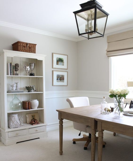 a French-inspired home office with two wooden desks, a neutral buffet for storage and a blakc metal pendant lamp