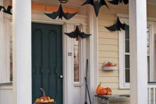 a Halloween porch with paper bats, natural orange pumpkins, brooms and fall leaves is a simple and cool idea