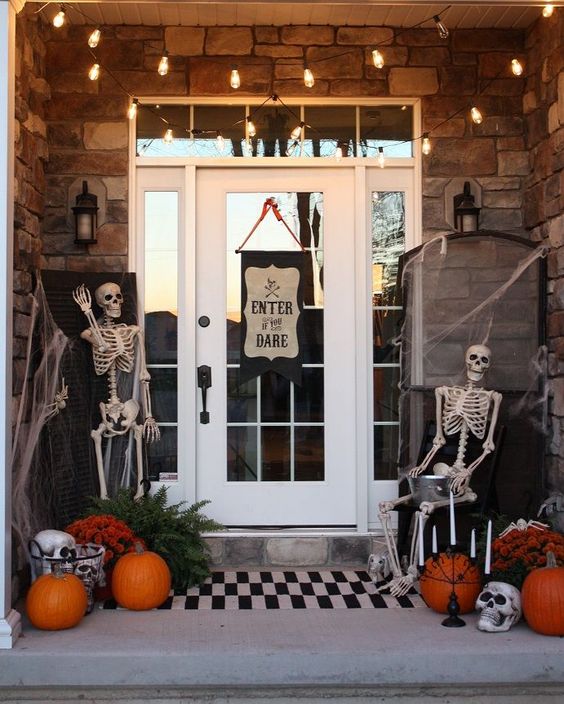 a Halloween porch with skeletons, spderwebs, orange pumpkins, skulls and candles plus a sign