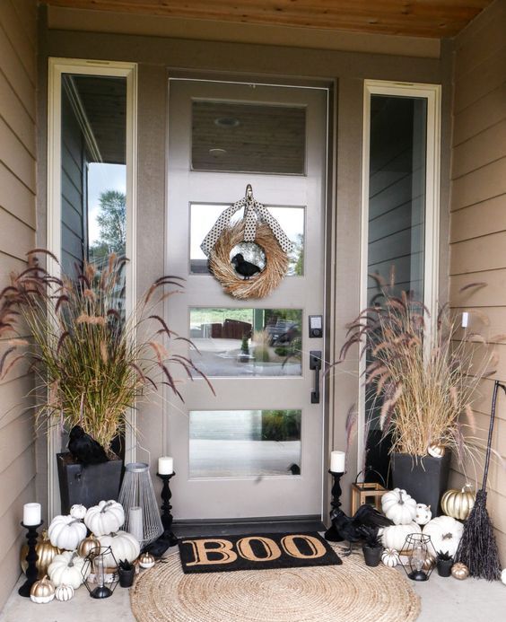 a Halloween porch with white and gilded pumpkins, candles, brooms, dried herbs and a wreath of wheat