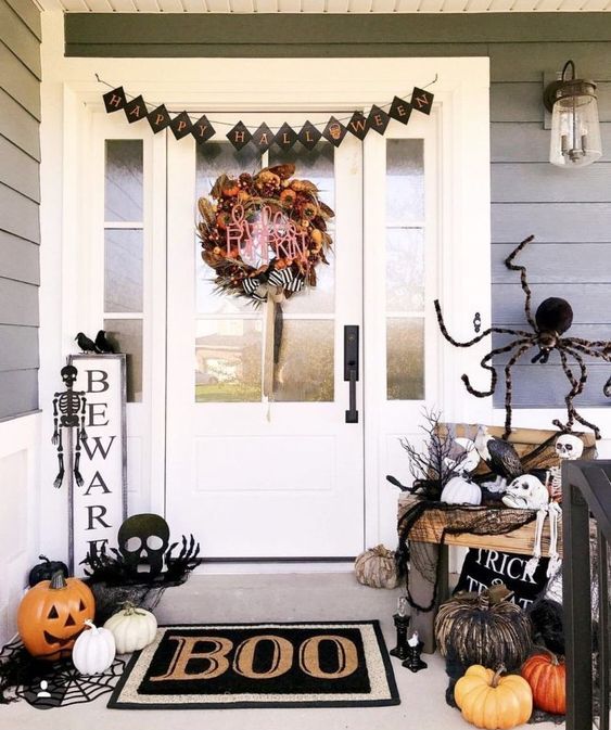a black and white Halloween porch with a bright wreath, a black bunting, skeletons and skulls, natural and faux pumpkins