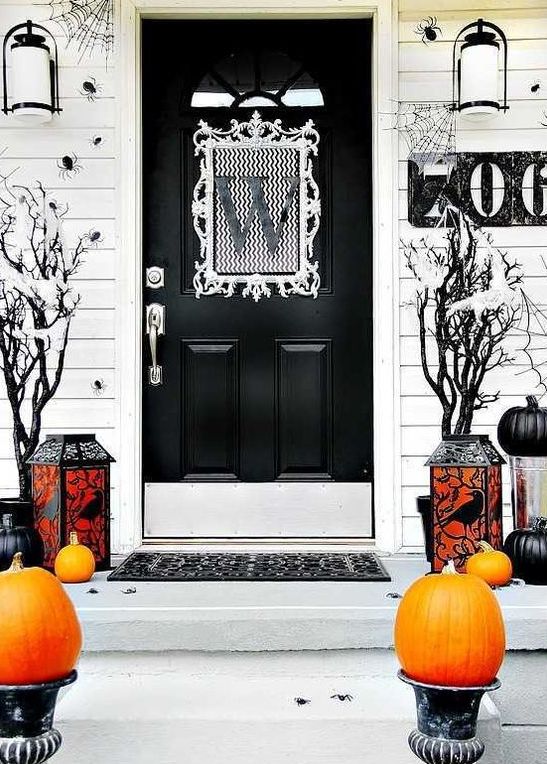 a black and white Halloween porch with orange and black pumpkins, candle lanterns and black trees plus spiders