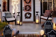 a bright Halloween porch with white pumpkins, candle lanterns, fake blackbirds, chalkboard signs, lights, skeletons and wreaths
