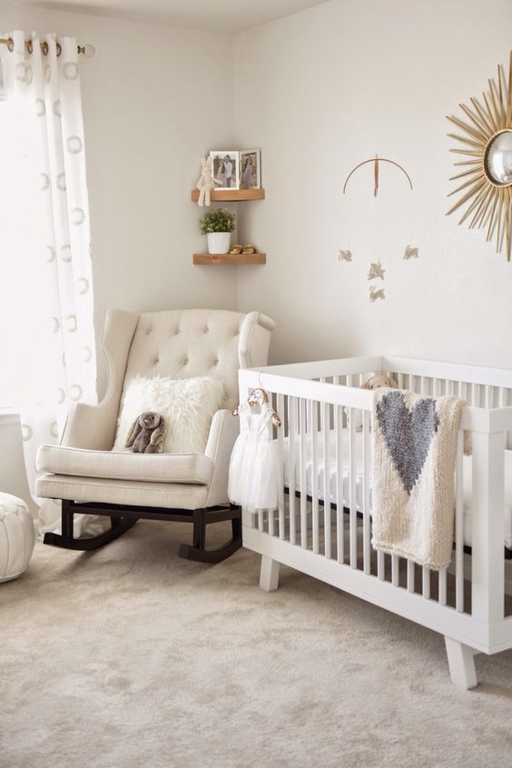 a chic neutral nursery with a rocker chair, a simple crib, a sunburst artwork, corner shelves and printed textiles