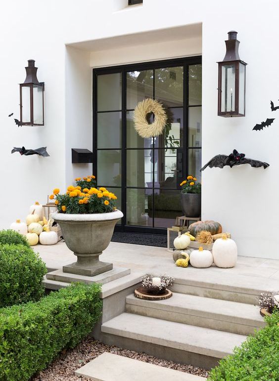 a contemporary Halloween porch with black bats, heirloom pumpkins, bold blooms and a wheat wreath