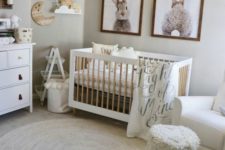 a cozy neutral nursery with artworks, a crib, layered rugs, a fringe stool and some simple wooden furniture