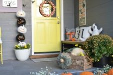 a cute and colorful Halloween porch with greenery, blooms, natural pumpkins, a ghost pillow, a buting, a wreath and a stack of pumpkins