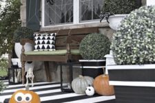 a fun black and white Halloween porch with a striped floor, natural pumpkins with faces, greenery, a spiderweb with spiders