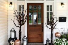 a gorgeous Halloween porch with painted and stenciled pumpkins, fall blooms in pots, black trees with lights and a large striped rug