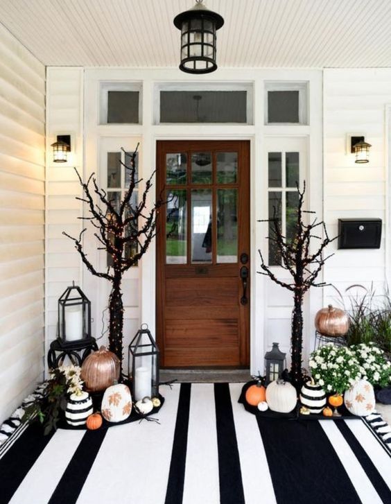 a gorgeous Halloween porch with painted and stenciled pumpkins, fall blooms in pots, black trees with lights and a large striped rug