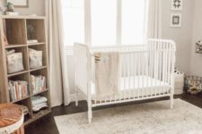 a light-filled neutral nursery with a crib, a wooden shelving unit, a printed rug, baskets and neutral curtains