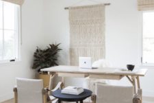a neutral and simple boho home office with woven shades and a macrame hanging, a minimal wooden desk and matching chairs plus a black side table