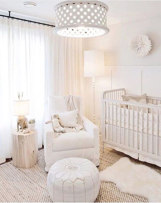 a neutral baby nursery with a jute rug, a white Moroccan pouf, a tree stump, a perforated lamp and a vintage crib