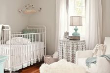 a neutral farmhouse nursery spruced up with mint touches, a printed rug, a fur ottoman, cozy vintage furniture