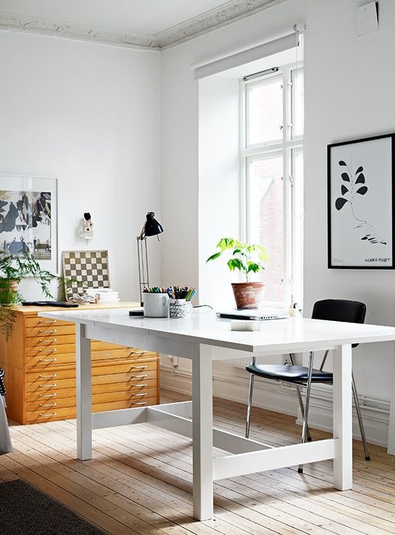 a neutral modern home office with a white desk, a wooden cabinet, some black and white art and a black chair