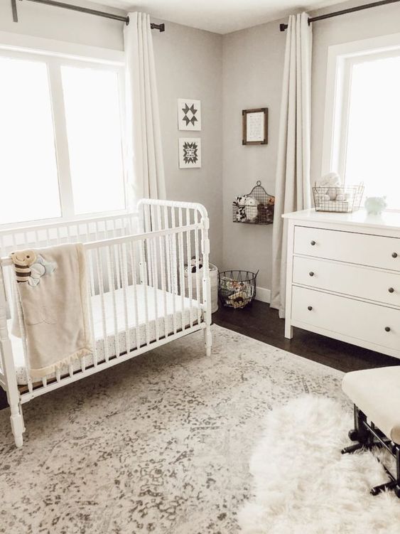 a neutral nursery with a printed rug, white furniture, wire basket shelves and storage units and artworks
