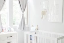 a neutral nursery with grey curtains, white furniture, layered rugs, a gallery wall with a toy head