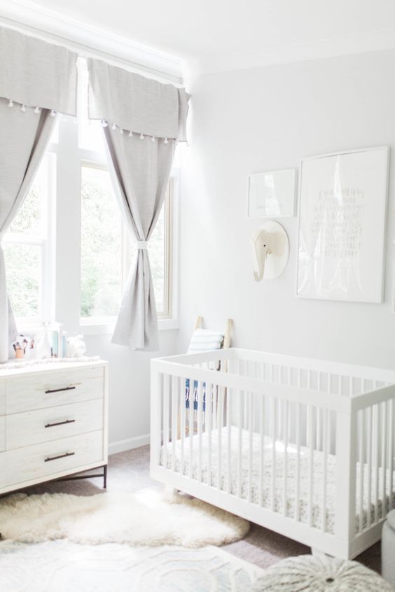 a neutral nursery with grey curtains, white furniture, layered rugs, a gallery wall with a toy head
