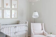 a peaceful nursery with a blush chair and a footrest, a beaded chandelier, a vintage crib and dresser and a gallery wall