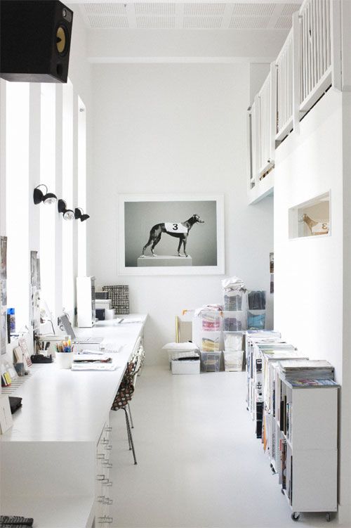 a shared white home office with lots of storage cabinets, a shared desk, some art and lamps and lots of light