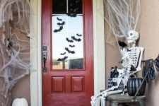 a simple and cool Halloween porch with spiderwebs, a skeleton, blackbirds, heirloom pumpkins and bats on the door