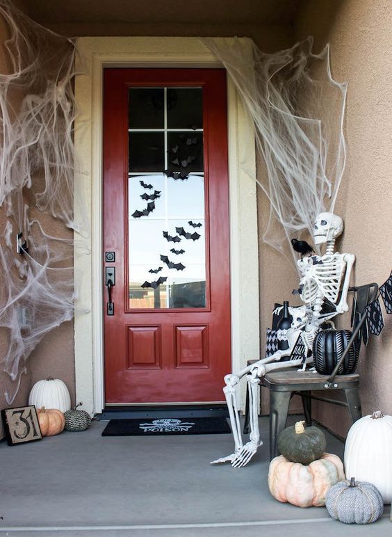 a simple and cool Halloween porch with spiderwebs, a skeleton, blackbirds, heirloom pumpkins and bats on the door