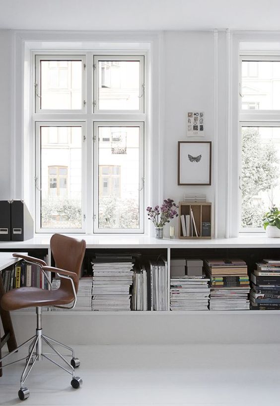 a simple minimalist white home office with a large open storag eunit, a white desk and a brown leather chair