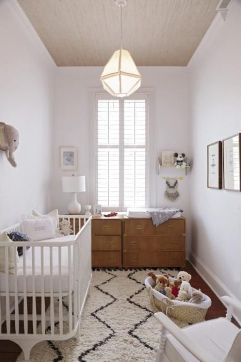 a small neutral nursery with a printed rug, wooden dressers, lots of toys and a faux elephant head on the wall