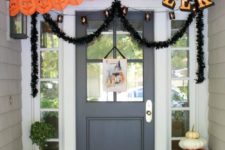 a whimsical Halloween porch with large black and orange paper decorations, natural pumpkins, candle lanterns and greenery