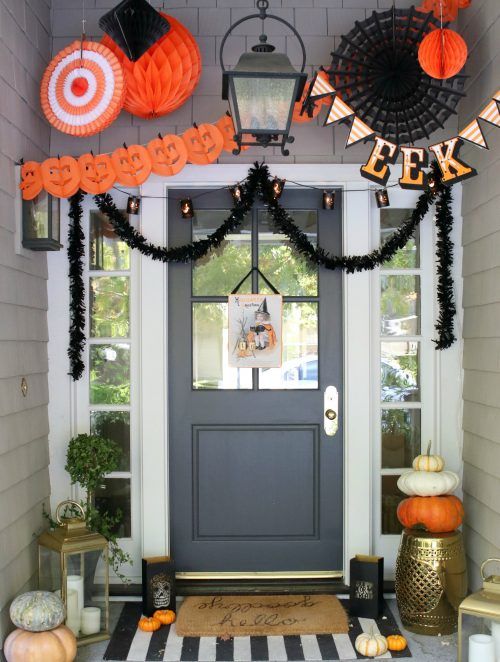 a whimsical Halloween porch with large black and orange paper decorations, natural pumpkins, candle lanterns and greenery