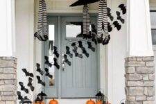a whimsy Halloween porch with witches’ legs and umbrellas, orange pumpkins, candle lanterns and bats