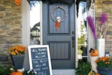 a whimsy and original Halloween porchh with skulls of paper, a skull wreath, natural pumpkins and bold fall blooms