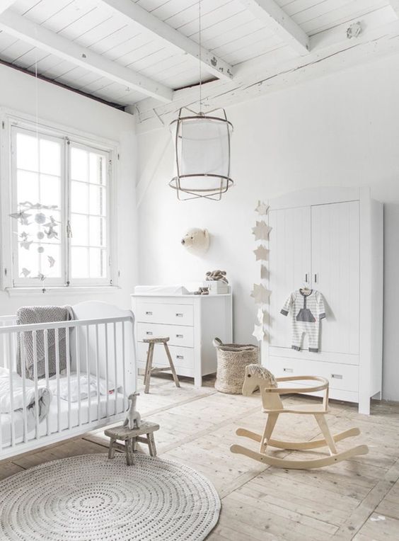 an airy neutral nursery with a cool rug, baskets, wooden stools, white storage furniture and a crib and a cool pendant lamp