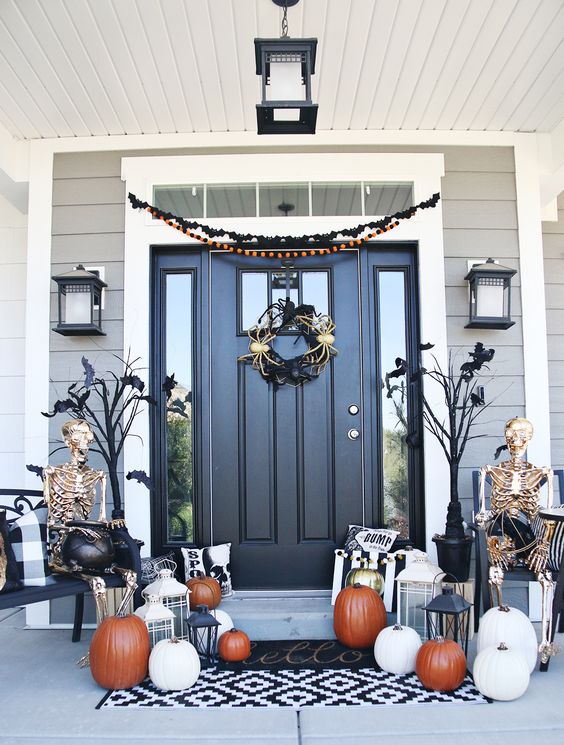 an elegant Halloween porch with gilded skeletons, orange and white pumpkins, candle lanterns and a wreath with spiders