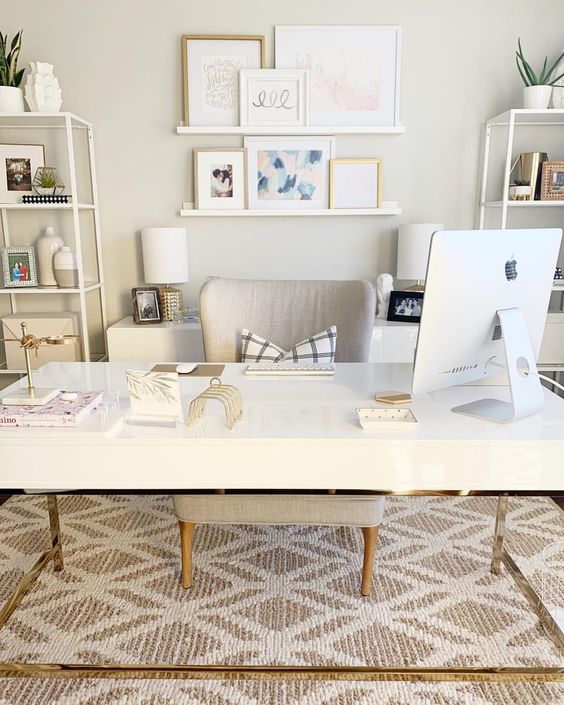 an elegant neutral home office with a large desk, storage units in white, cabinets, a gallery wall on ledges and a comfy chair