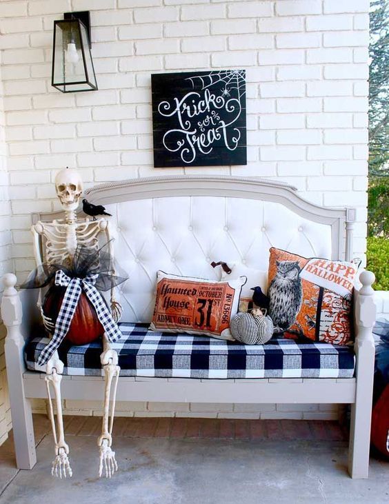 an upholstered bench with Halloween pillows, a skeleton with a pumpkin and a bow atop, a sign and a candle lantern