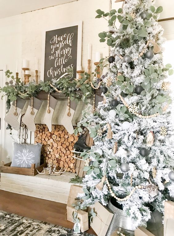 a neutral Christmas tree with black, grey and white ornaments and wooden beads, a fireplace with greenery and wooden beads, striped stockings and antlers