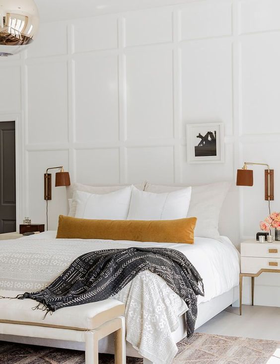 a neutral bedroom with paneling, chic neutral furniture, elegant leather sconces and a printed rug looks welcoming