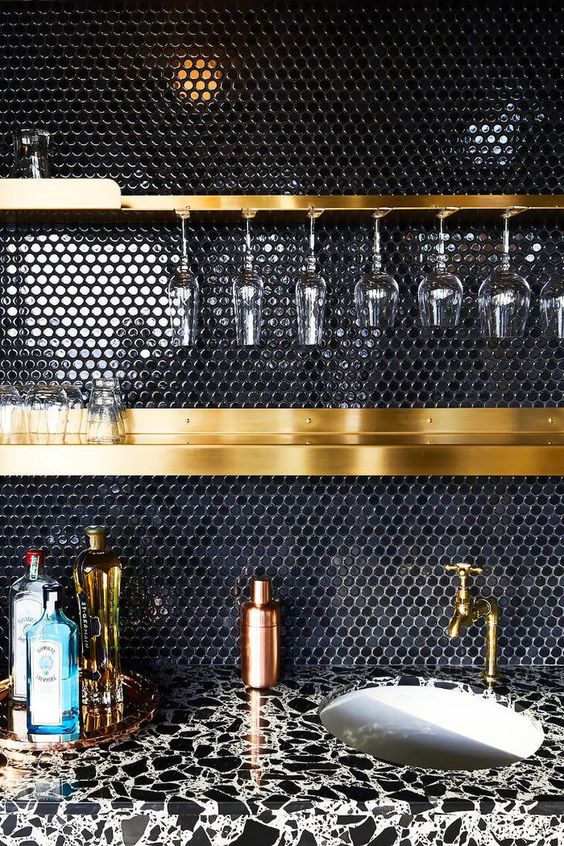 a black penny tile backsplash and gold shelves and fixtures make up a very chic and refined combo