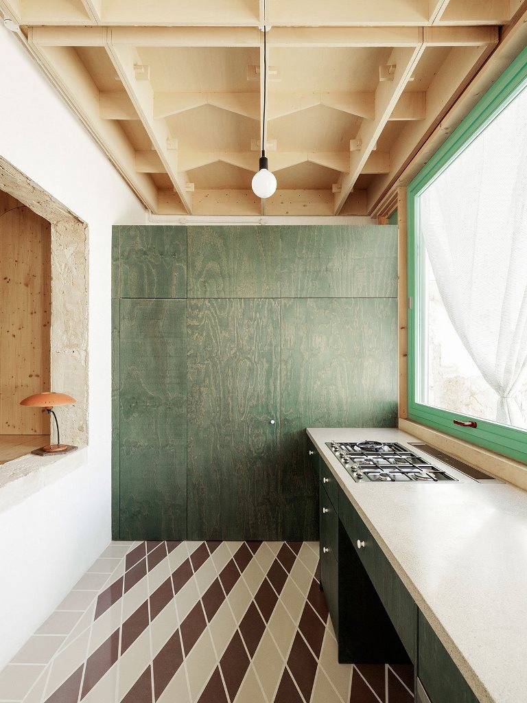 The kitchen is done with tiles and dark green plywood cabinets and a large kitchen island