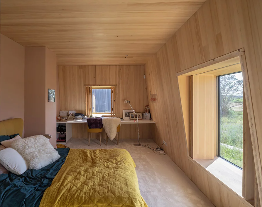 This bedroom is done with plywood completely, there are large windows, a mini home office in the corner and a large bed