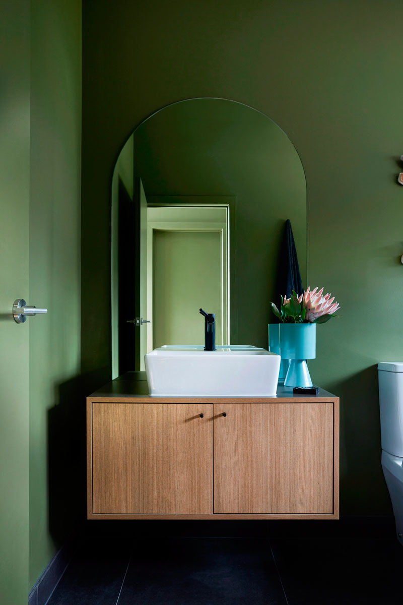 The bathroom is also done with green walls, a floating vanity and a square sink plus dark fixtures
