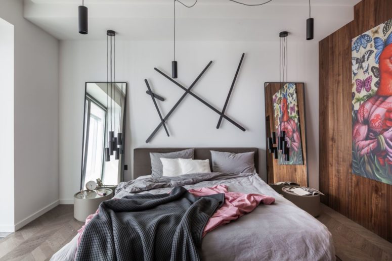 The bedroom is modern and whimsy, wih a bed, a creative artwork, pendant lamps, mini nightstands and a mirror