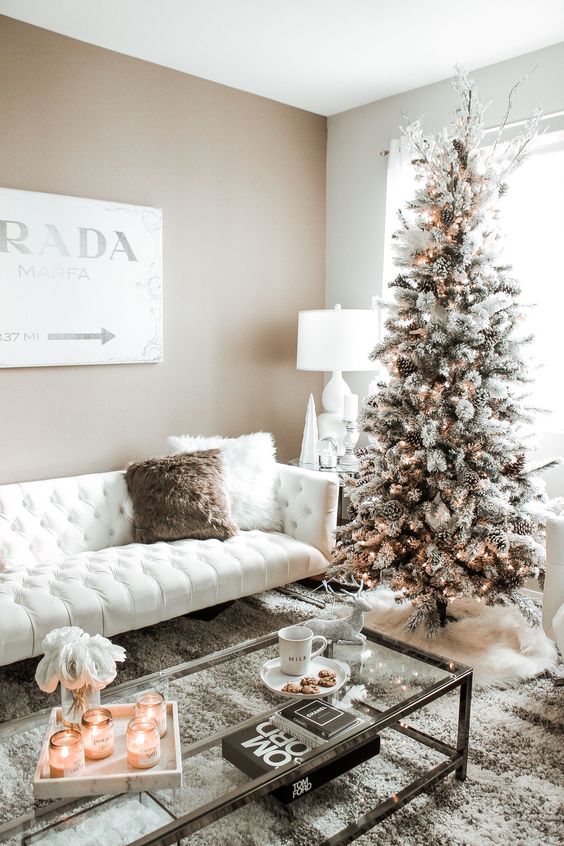 a snowy Christmas tree with pinecones and lights and some white branches on top, candles and fluffy pillows