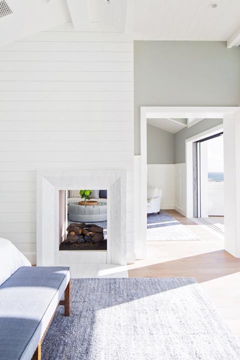 A coastal home with a double sided fireplace that is clad with shiplap and brings coziness to the neutral spaces
