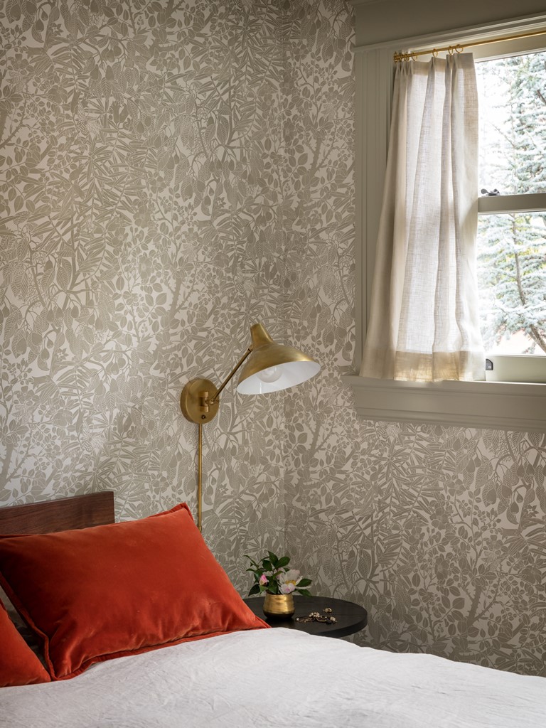 Another bedroom is done with grey printed wallpaper, rust pillows and brass touches