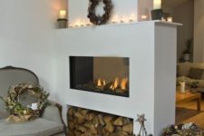 09 a sleek white fireplace with firewood storage, candles on the mantel and a wreath with pinecones for winter
