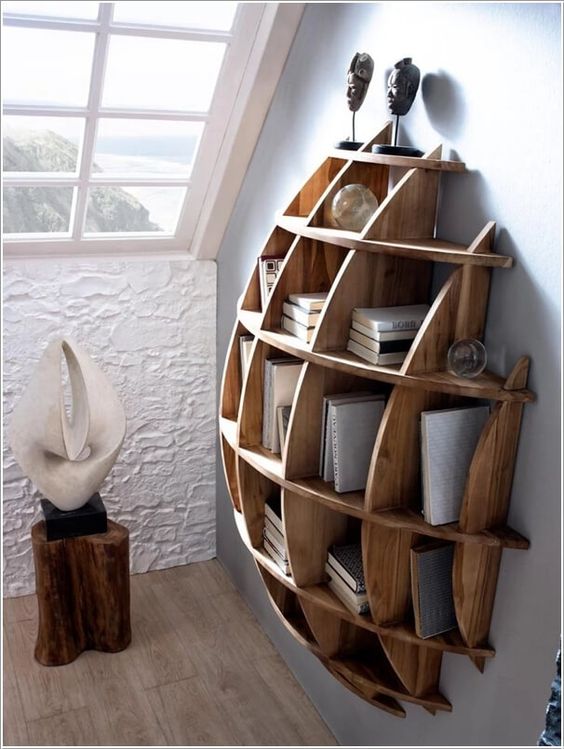 A creative semi circular wooden shelving unit with books and sculptures is art itself