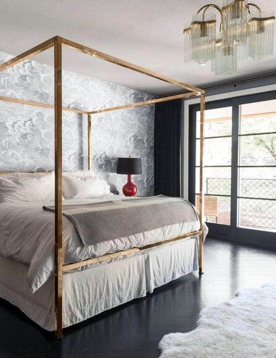 a glam brass canopy bed, an echoing chandelier and shiny black floors add chic and glam to the bedroom