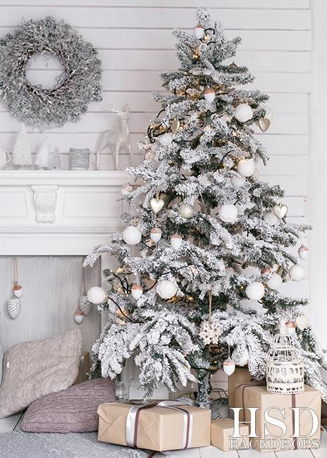 a neutral winter nook with a flocked Christmas tree with white ornaments, a snowy wreath on the wall, a white fireplace and pastel pillows